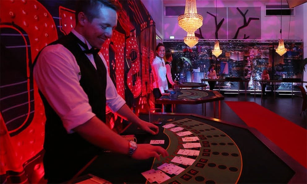 Dealer i aktion ved blackjack-bordet med Vegas-kulisse og lysekroner